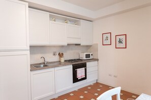 Una cocina compacta con armarios blancos, un lavamanos, un microondas y una estufa. Hay dos cuadros en la pared.