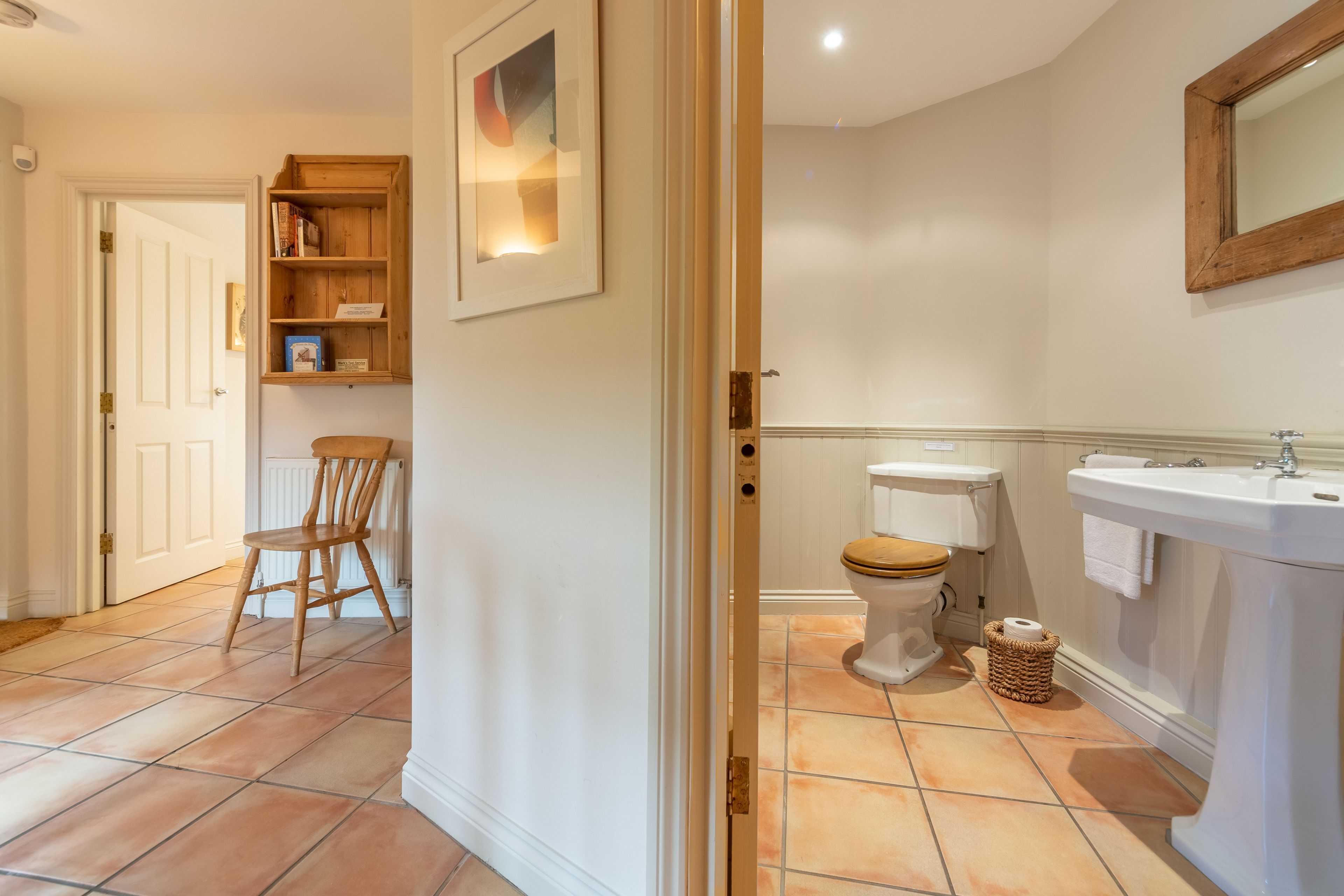 A bathroom with a toilet, sink, and wooden chair.
