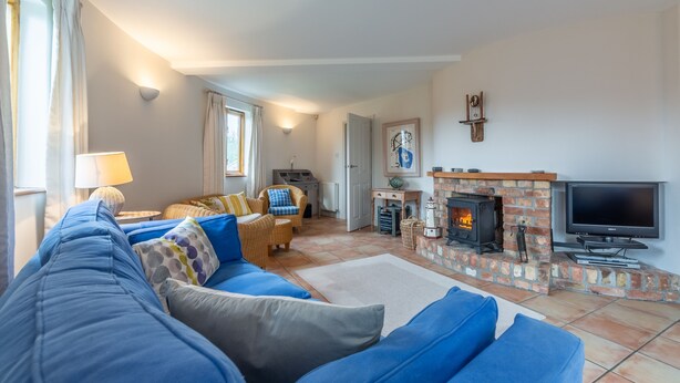 A living room with a blue sofa, a television, a fireplace, and a wicker chair. - The Roundhouse has an unusual design and stands alone overlooking the lakes. (Wadebridge)