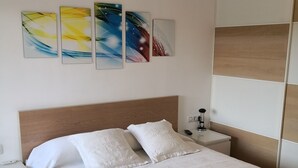 A neatly made bed with white linens and pillows, a wooden headboard, a bedside table with a lamp, and abstract wall art. - AIR CONDITIONING, POOL, BARBECUE,PARKING,WI-FI. PERFECT FOR FAMILIES AND COUPLES (Platja d'Aro)