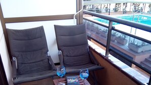 A balcony with two grey cushioned chairs, a small wooden table with two glasses of blue liquid, and a book titled "Porters". - AIR CONDITIONING, POOL, BARBECUE,PARKING,WI-FI. PERFECT FOR FAMILIES AND COUPLES (Platja d'Aro)