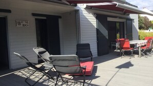 Une terrasse extérieure couverte, avec une table et des chaises, une chaise pliante et un panneau indiquant : « WHAT THE BEACH ».