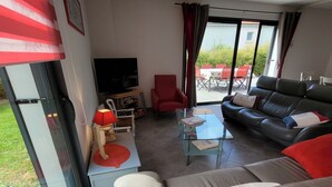 Un salon moderne avec un canapé, un fauteuil rouge, une table basse en verre et un téléviseur.