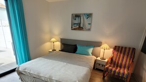 Une chambre à coucher avec un grand lit, deux tables de chevet avec des lampes, une chaise colorée et un tableau au mur.
