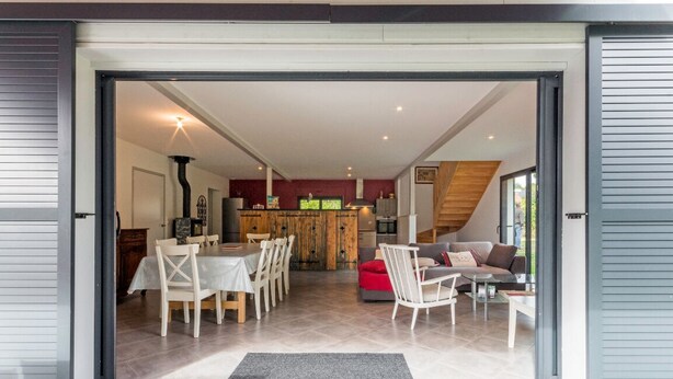Une porte ouverte donne sur un espace repas comprenant une table et des chaises, un canapé et, au fond, une cuisine.