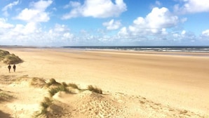 Une vaste plage de sable, bordée de dunes, et un ciel bleu dégagé.