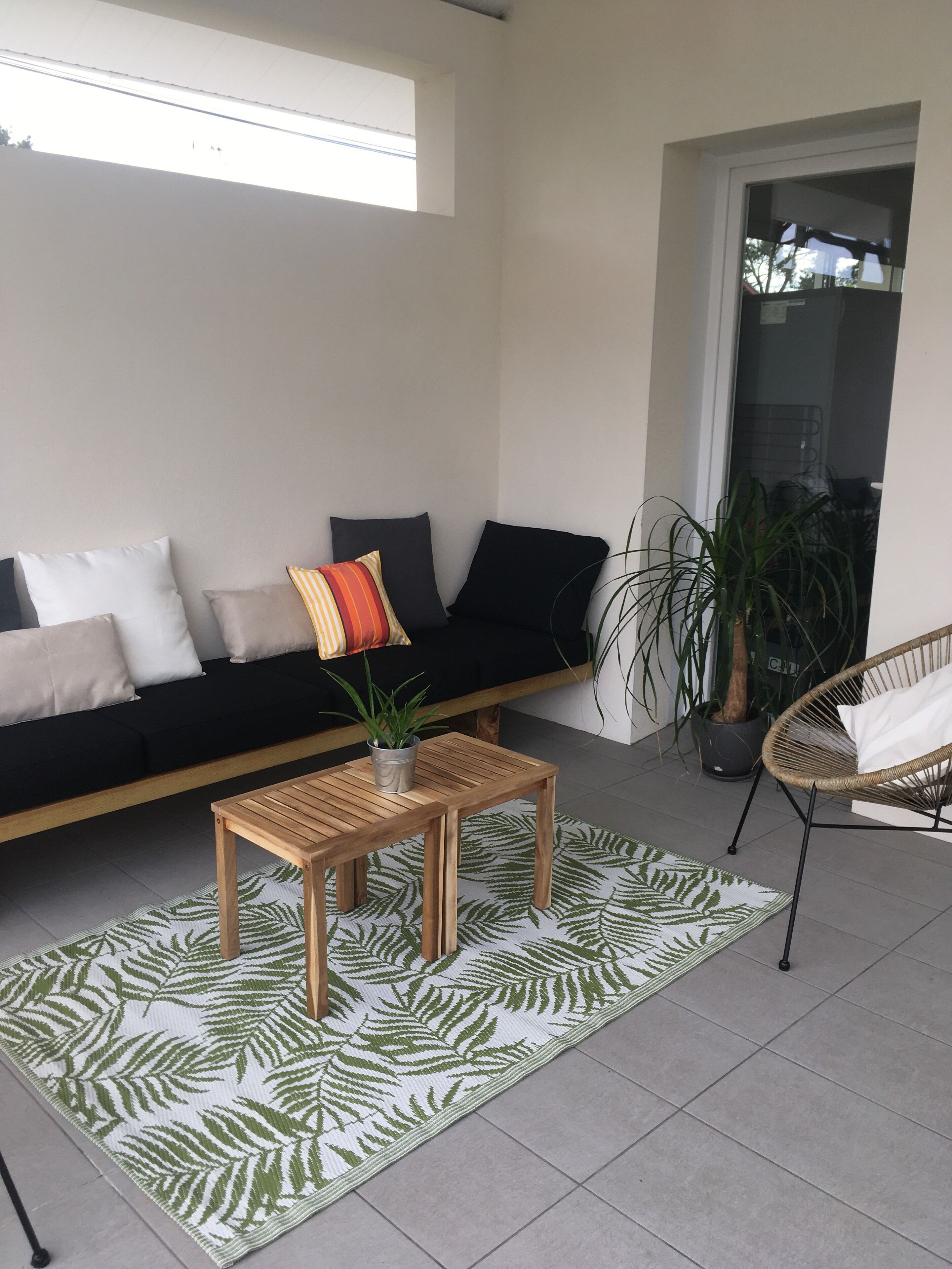 Un salon moderne avec un canapé noir, une table basse en bois et un tapis à motifs de feuilles vertes.