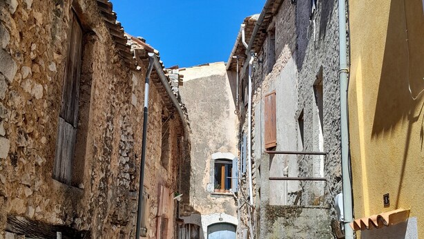Una calle estrecha con edificios de piedra, una puerta verde y una puerta azul.