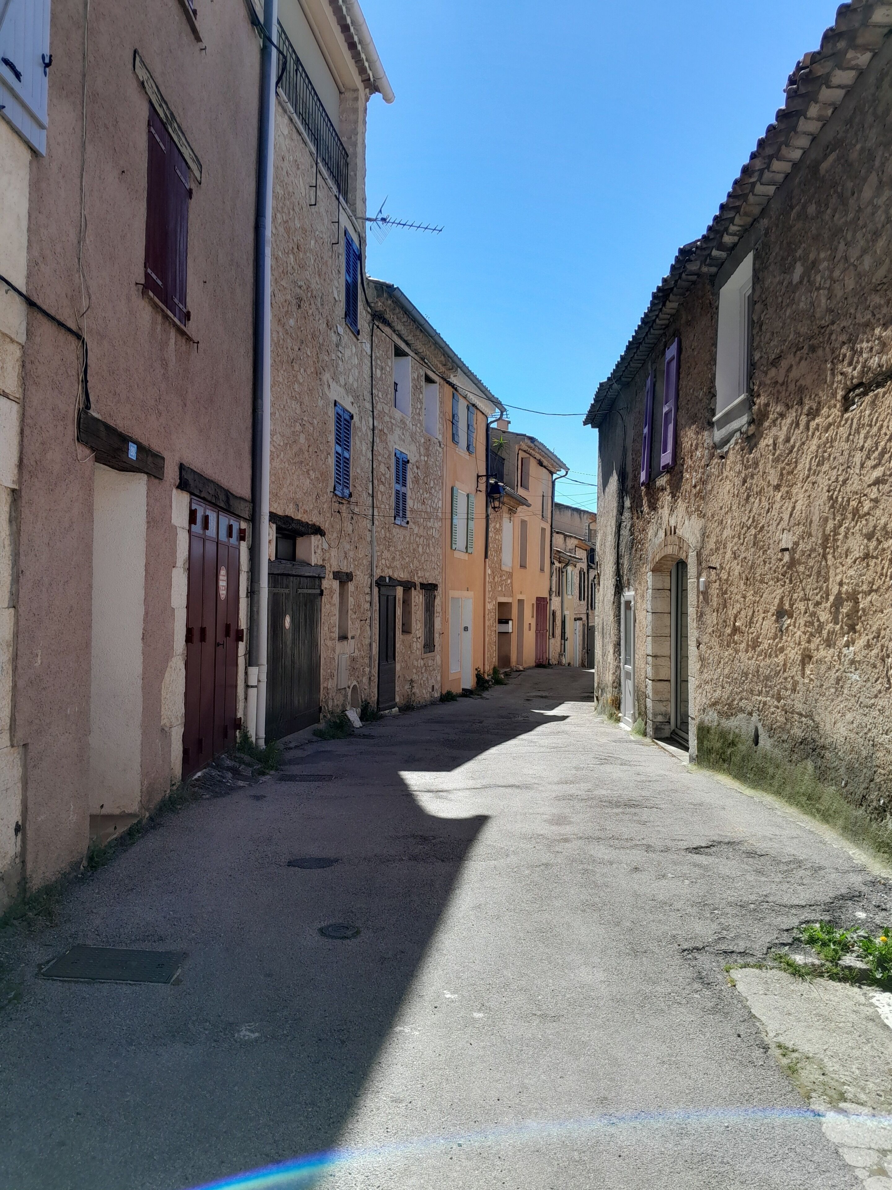 Une rue étroite bordée de bâtiments historiques, dont certains présentent des portes et des fenêtres apparentes, sous un ciel dégagé.