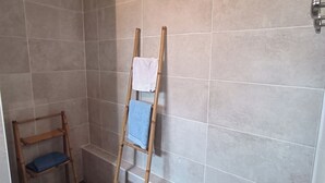 Un baño con baldosas color beige, una escalera de madera y una toalla azul en el suelo.