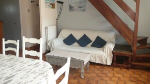 Una sala de estar acogedora con un sofá blanco, una escalera de madera y piso de baldosas.