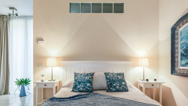 A bedroom with a bed, two bedside tables with lamps, a potted plant, and a painting on the wall. - Bright and spacious, in the picturesque setting of a former cinema (Bologna)