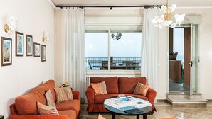 Olohuoneessa on kaksi oranssia sohvaa, sohvapöytä ja suuri ikkuna, josta avautuu näkymä merelle.