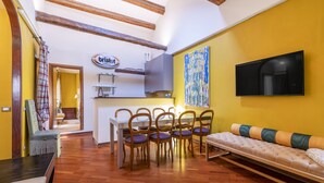 A dining area with a wooden table and chairs, a sofa, and a TV mounted on the wall.