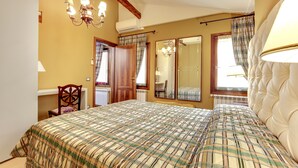 A bedroom with a large bed, a wooden chair, a mirror, and a chandelier.