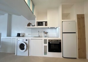 A compact kitchen with a washing machine, microwave, oven, and a refrigerator. - Beachfront apartment with private garden, wifi and parking space (Jávea)