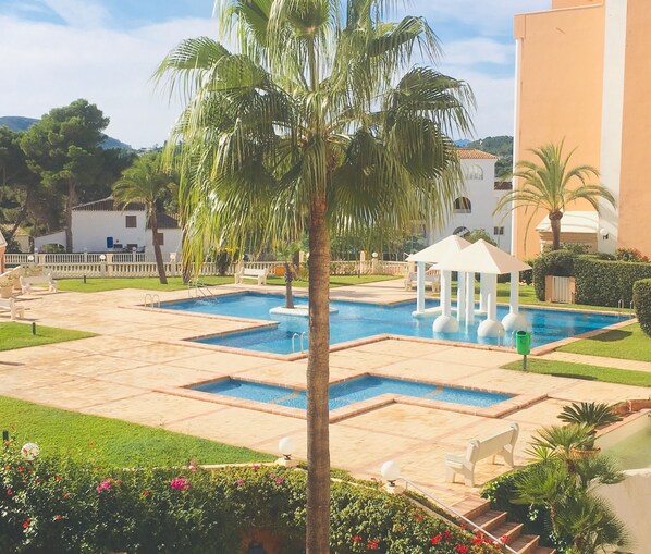A pool area with multiple pools, palm trees, and a gazebo. - Beachfront apartment with private garden, wifi and parking space (Jávea)