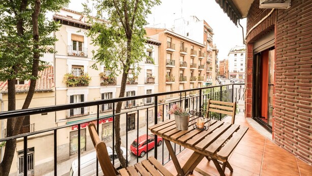 Ein Balkon mit Holzmöbeln, einem Blumentopf und Blick auf die Straße darunter.