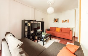A living room with a sofa, a coffee table, a TV on a black stand, and a red sofa. - Spacious apartment with terrace. 3bed in the center (Madrid)