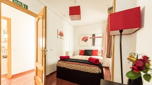 Ein Hotelzimmer mit einem Bett, einem Nachttisch, einer roten Lampe, einer Vase mit Blumen und einer Tür mit einem Schild.