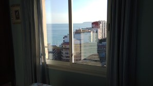 Ein Schlafzimmer mit einem Bett, einem Fenster mit Vorhängen und Blick auf Gebäude und Wasser.