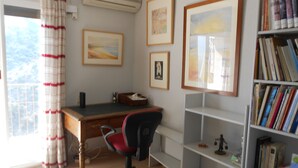 Ein Zimmer mit Schreibtisch, Stuhl, Bücherregal und Bildern an den Wänden.