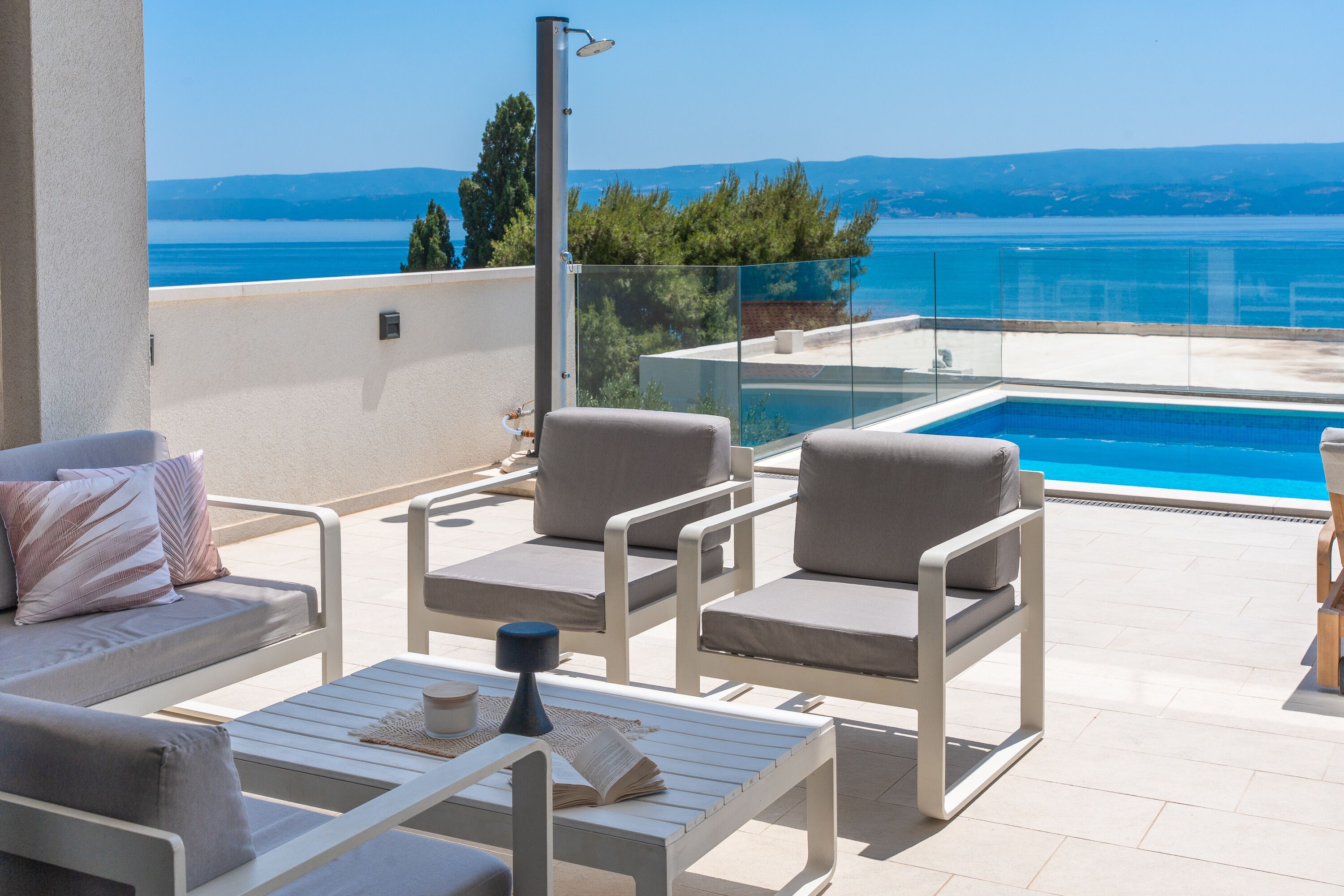 A balcony with a pool, white furniture, and a view of the sea.