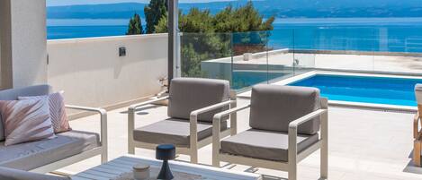A balcony with a pool, white furniture, and a view of the sea.