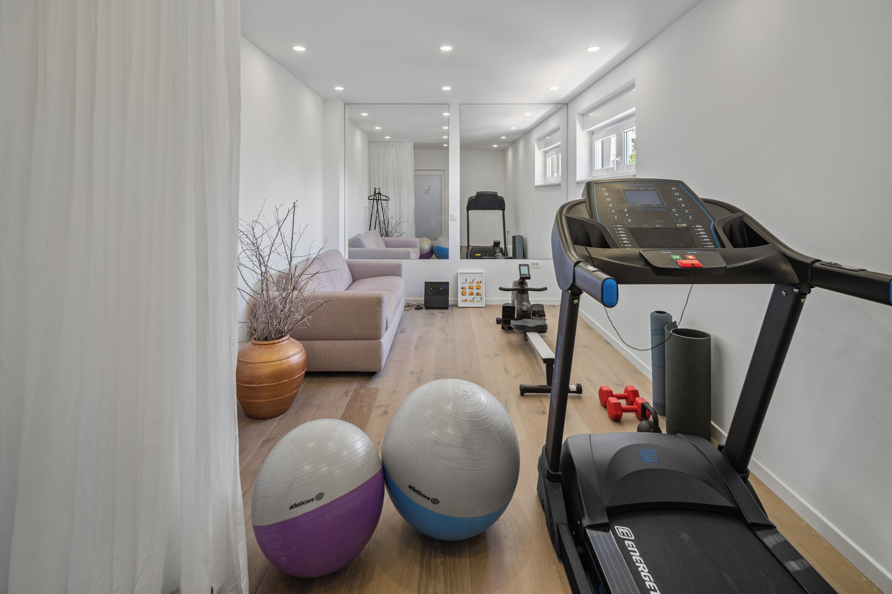 Une salle de sport à domicile équipée d’un tapis de course, de ballons d’exercice et d’haltères.