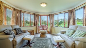 Un salon spacieux avec deux canapés beige, un tapis à motifs et de grandes fenêtres donnant sur l’extérieur.