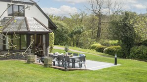 Une maison dotée d’un patio comprenant une table et des chaises, le tout entouré d’une pelouse bien entretenue et d’arbres.