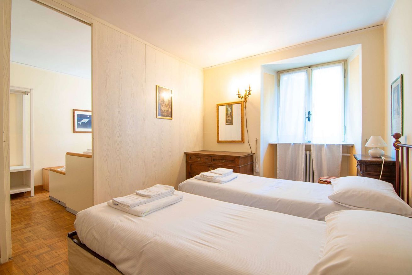 A hotel room with two beds, a wooden dresser, a mirror, and a window with curtains.