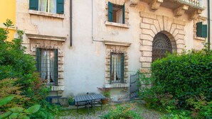 Ein Innenhof mit einem Steinhaus, einer Bank und üppigem Grün.