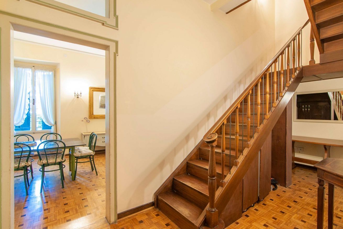 A wooden staircase leading to an upper floor, a dining area with chairs and a table, and a window with curtains.