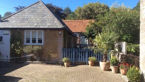 A house with a tiled roof, a wooden fence, and potted plants. - 17th Century converted Coach House in Shaftesbury, Dorset (Shaftesbury)