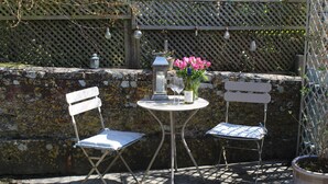 An outdoor seating area with two white folding chairs, a small round table, a candle, a wine glass, and a vase with pink flowers. - 17th Century converted Coach House in Shaftesbury, Dorset (Shaftesbury)