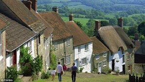 A traditional stone building with a steep roof, surrounded by lush green fields and a distant view of rolling hills. - 17th Century converted Coach House in Shaftesbury, Dorset (Shaftesbury)