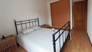 A bedroom with a bed, wooden floor, a wardrobe, and a door. - Holiday Home in Sines (Sines)