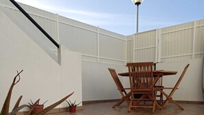 A rooftop patio with a wooden table and chairs, potted plants, and a metal lamp post. - Holiday Home in Sines (Sines)