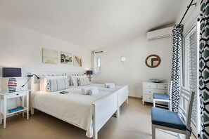 Un dormitorio con cama, mesitas de noche, una silla, un espejo y una ventana con cortinas.