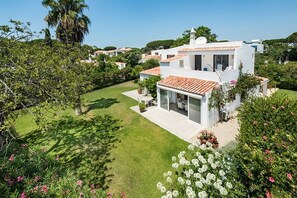 Una villa moderna con un patio amplio, rodeada de exuberante vegetación y un césped cuidado.