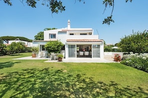 A two-story house with a patio area, a covered seating space, and a garden.