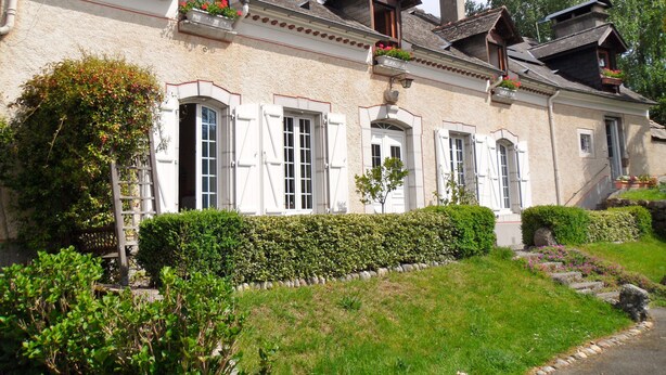 En traditionel bygning i europæisk stil med mange vinduer, en stenfassade og en velplejet have med hække og blomster.