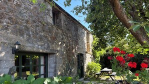 Un edificio de piedra rústico con jardín, flores rojas y una mesa de madera.