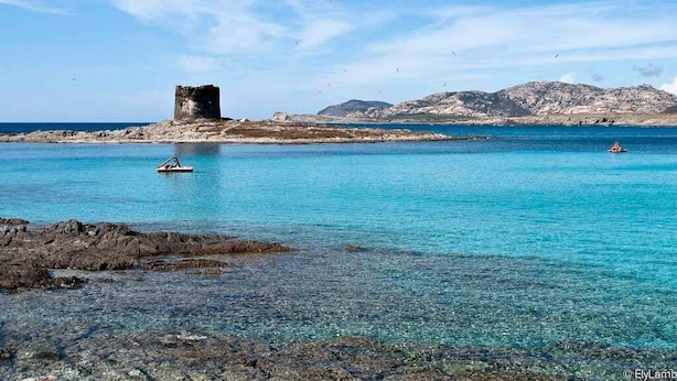 Een kustgezicht met helder turquoise water, een rotsachtige kustlijn en een historisch torentje.