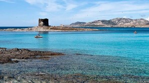 A coastal scene with clear turquoise waters, a rocky shoreline, and a historical tower structure.