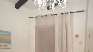 Un dormitorio con una cama, una silla, un cuadro y una cortina.