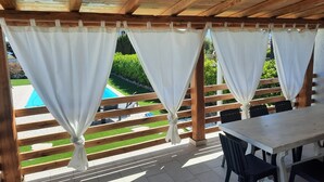 Un espacio de estar al aire libre cubierto con vista a la piscina, vigas de madera y una mesa con sillas.