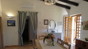 Un comedor con una mesa de madera, sillas, un jarrón de flores, un espejo y vistas al exterior por una puerta de madera.