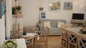 Una sala de estar acogedora con sofá, una mesa de comedor con sillas, televisor y obras de arte en las paredes.